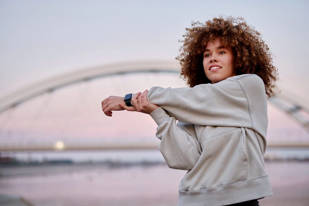 Young woman stretching her arm before running near a bridge